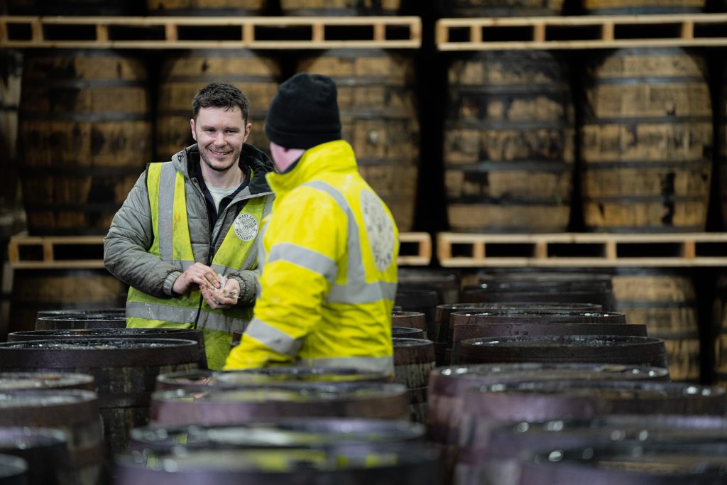 Two West Cork Distillery team members sharing a laugh between rows of maturing casks in the warehouse