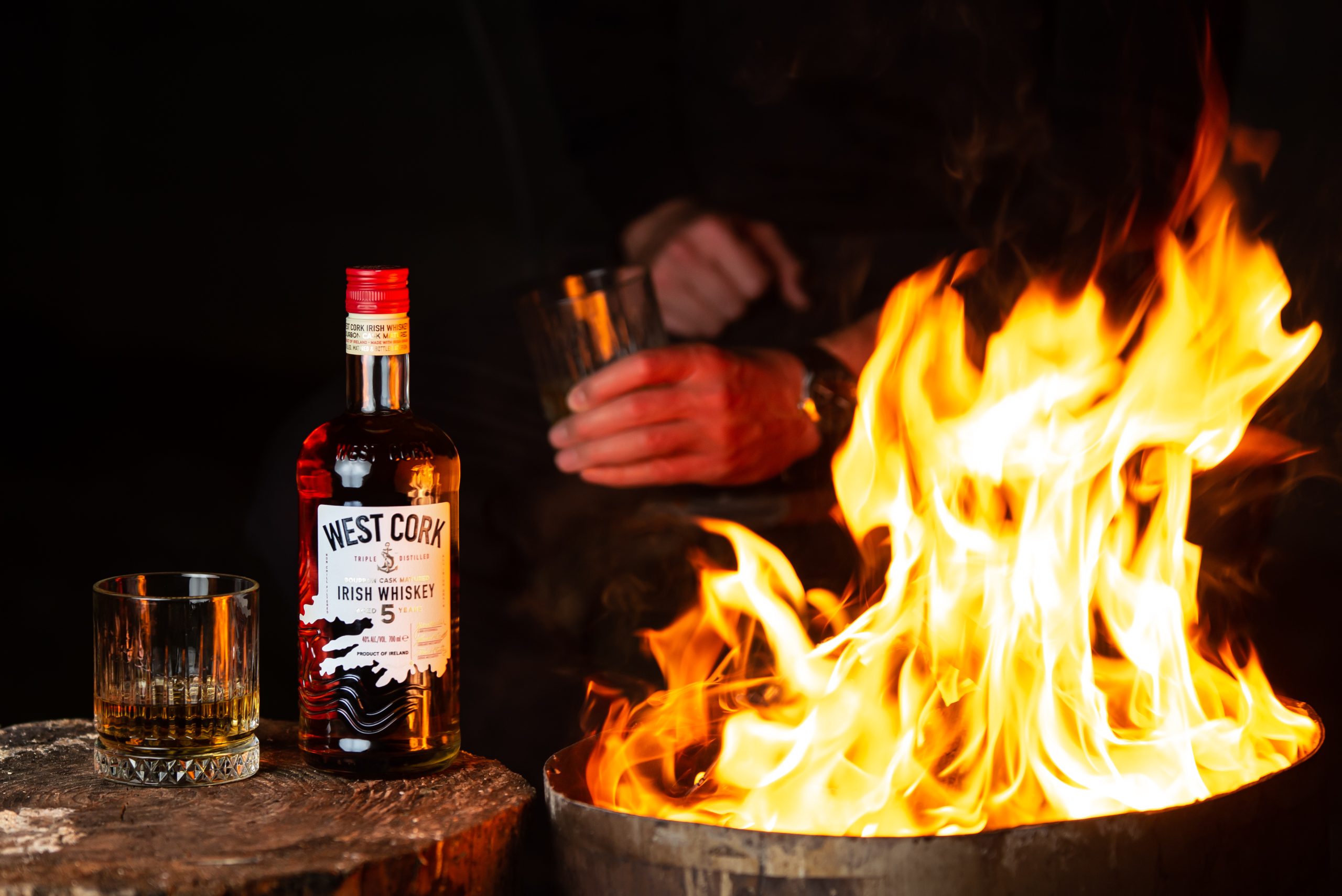 A West Cork Irish Whiskey bottle and dram beside a fire pit